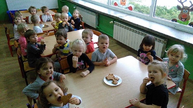 Na zdjęciu przedszkolaki siedzą przy stolikach, jedzą pierniczki.