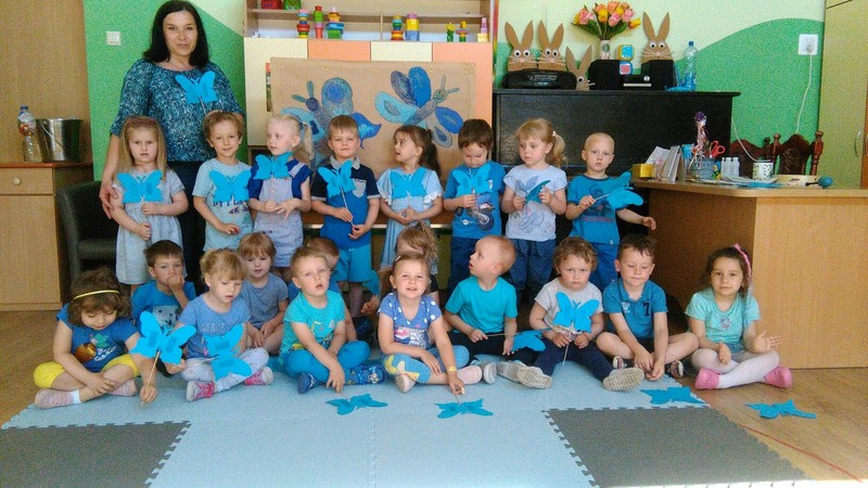 Zdjęcie przedstawia grupę Wróbelki ubraną w niebieskie kolory. Dzieci trzymają w dłoni papierowe motyle. Przedszkolaki jednoczą się z ludźmi z autyzmem. 