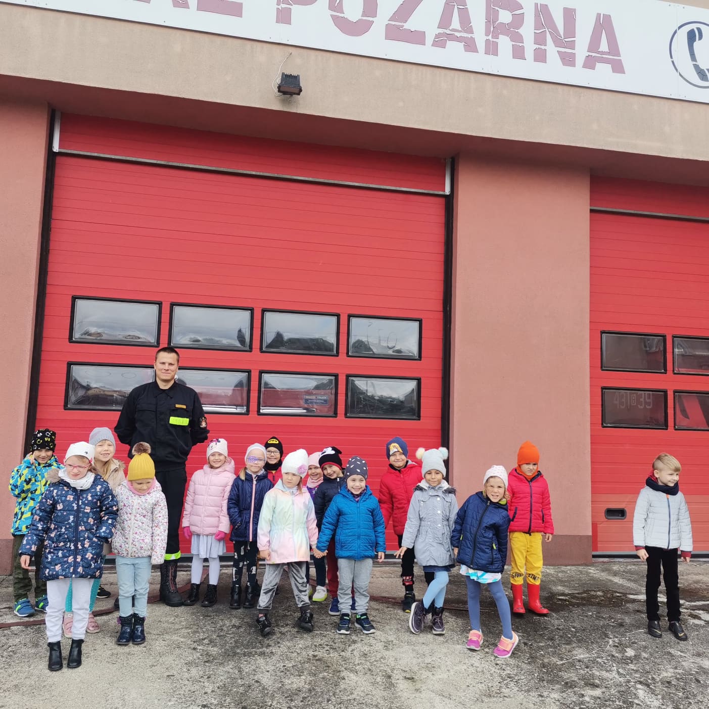 Grupa dzieci stoi przed budynkiem straży pożarnej w mieście Hajnówka.