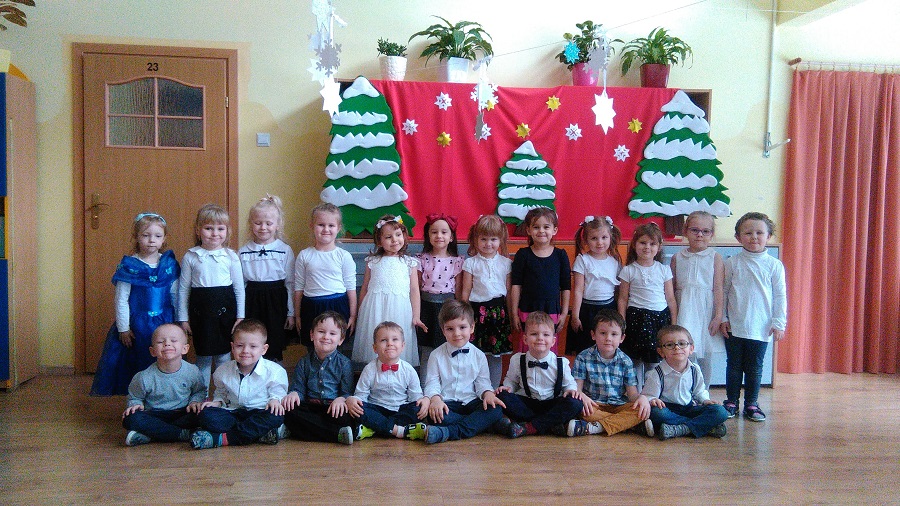 Zdjęcie grupowe dzieci ubranych na galowo. W tle widać zimową dekoraję.