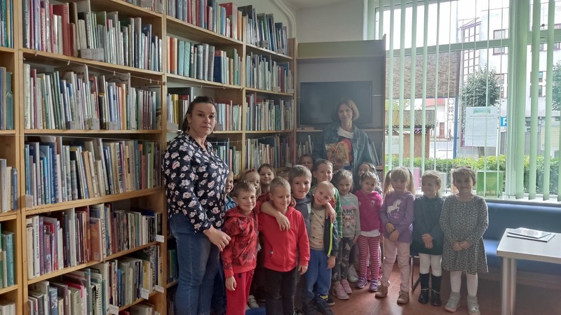 Grupa dzieci z opiekunem przy półkach z zksiążkami w bibliotece