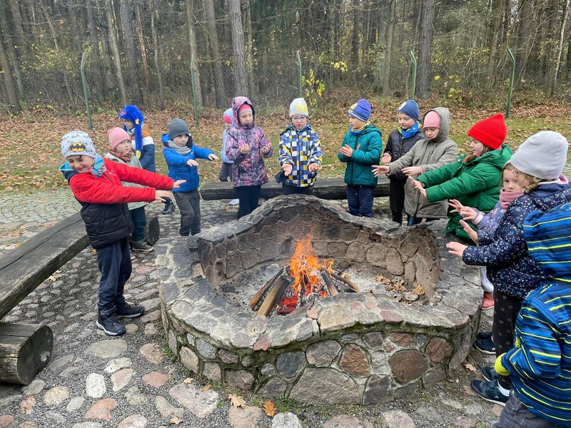 Dzieci z grupy Sówek smażą kiełbaski nad ogniskiem.