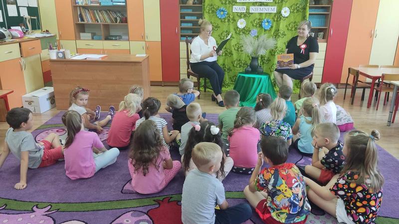 dzieci siedza na podłodze i słuchają powieści czytanej przez dorosłych