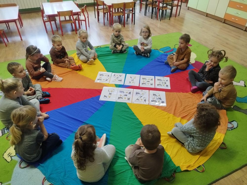 dzieci siedzą w koło na kolorowej macie. Układają puzle