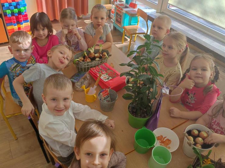 Dzieci siedzą wokół stołu na którym stoją doniczki z roślinami