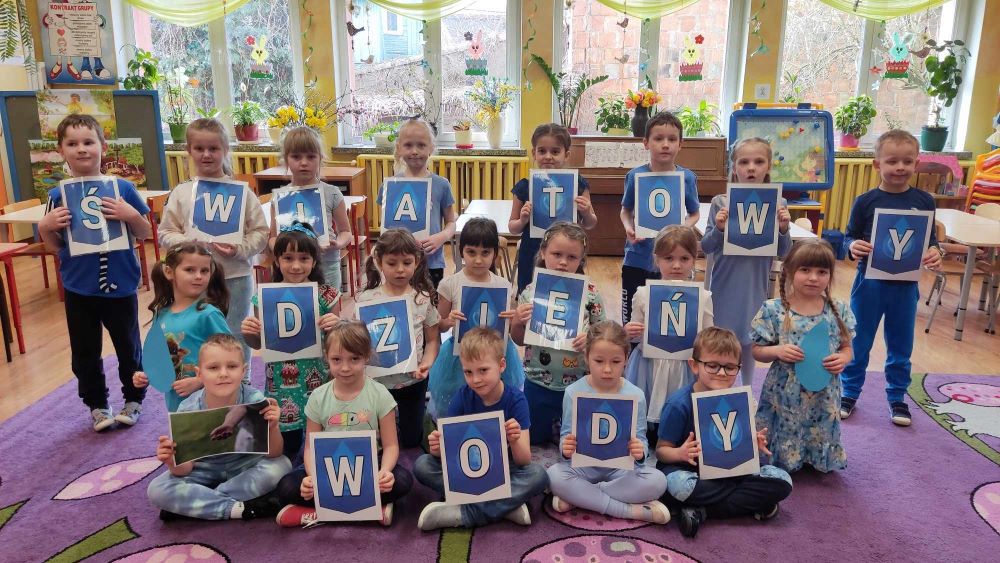 Dzieci pozują do zdjęcia, w rękach trzymają niebieskie kartki z literami.